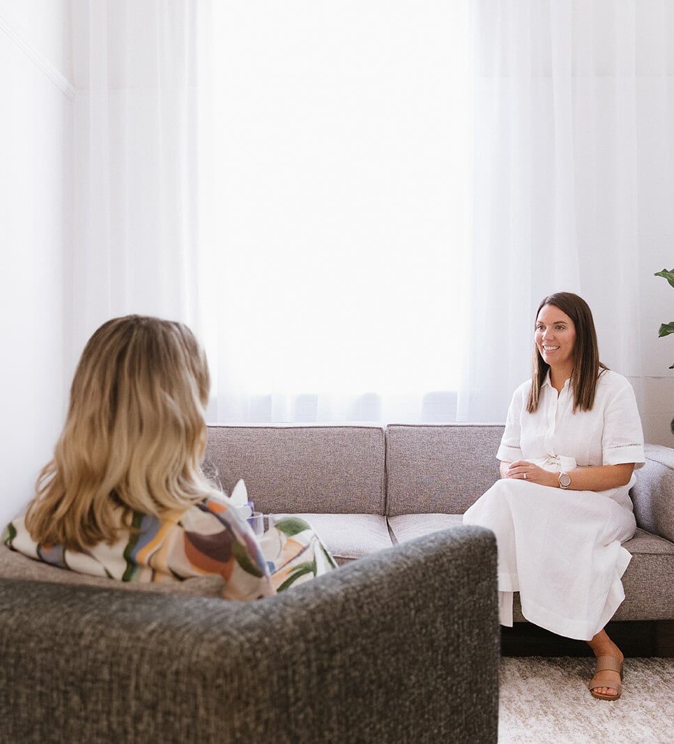 A psychologist and client in conversation in a bright, softly furnished therapy room.
